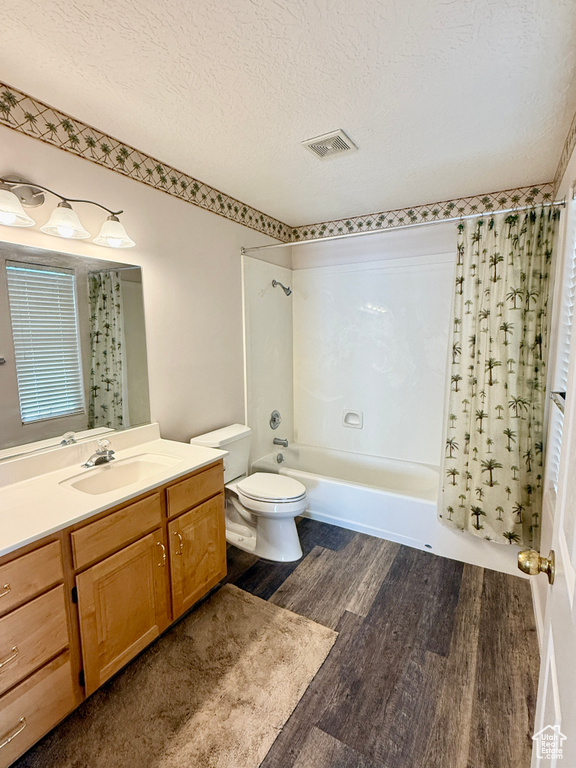 Full bath with a textured ceiling, visible vents, wood finished floors, vanity, and tub / shower combination