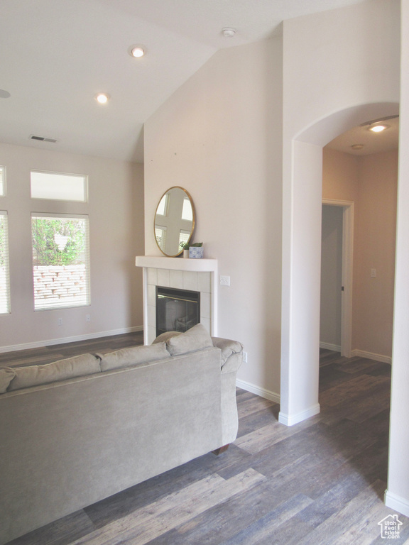Unfurnished living room with visible vents, a tiled fireplace, arched walkways, vaulted ceiling, and wood finished floors