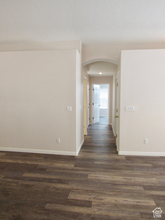 Hall with a textured ceiling, arched walkways, dark wood-type flooring, and baseboards