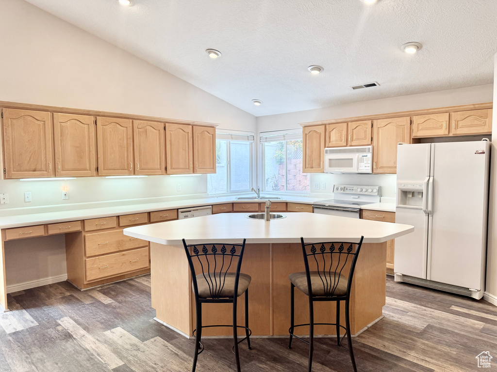Kitchen with an island with sink, lofted ceiling, white appliances, and light brown cabinets