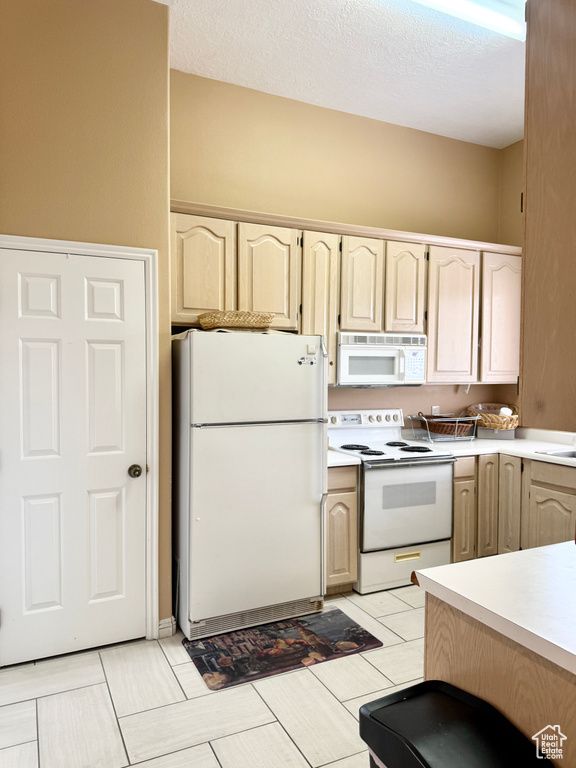 Kitchen featuring light countertops, a textured ceiling, light brown cabinets, and white appliances