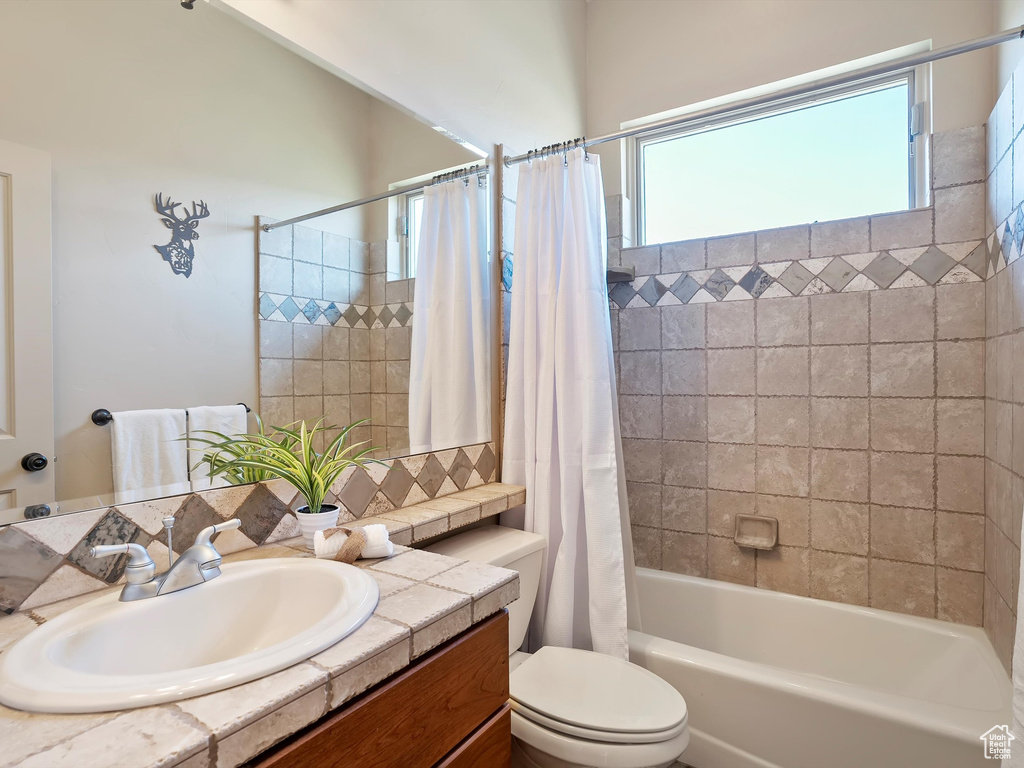 Bathroom featuring toilet, shower / tub combo, decorative backsplash, and vanity
