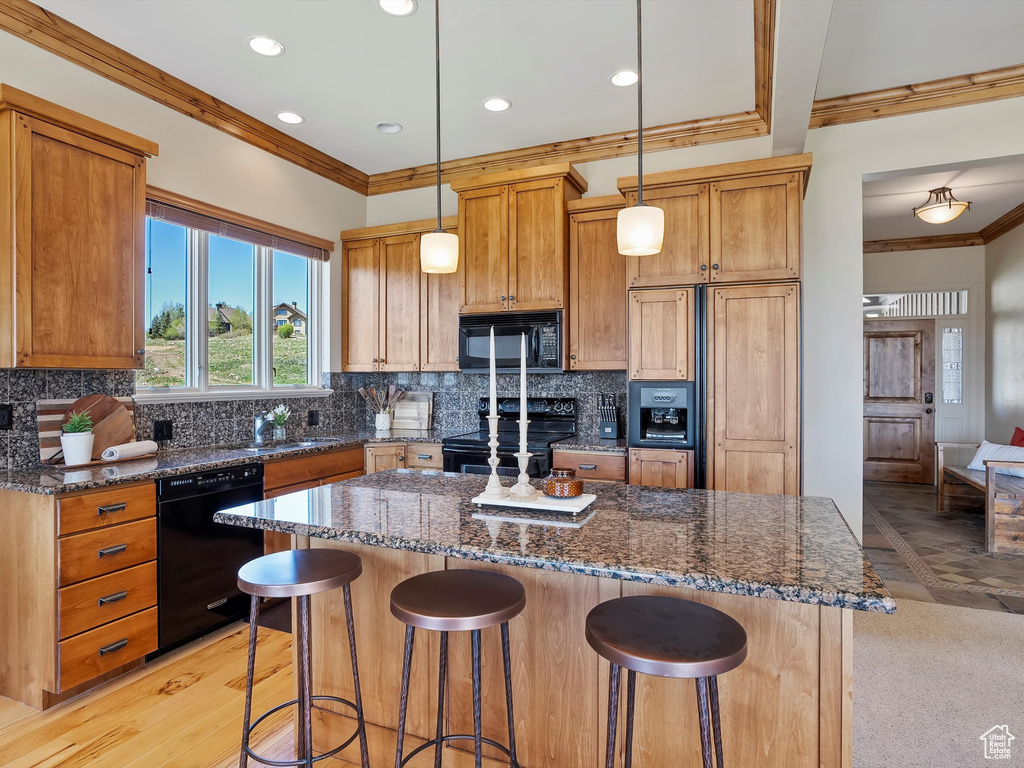 Kitchen featuring dark stone counters, ornamental molding, a kitchen breakfast bar, black appliances, and a kitchen island
