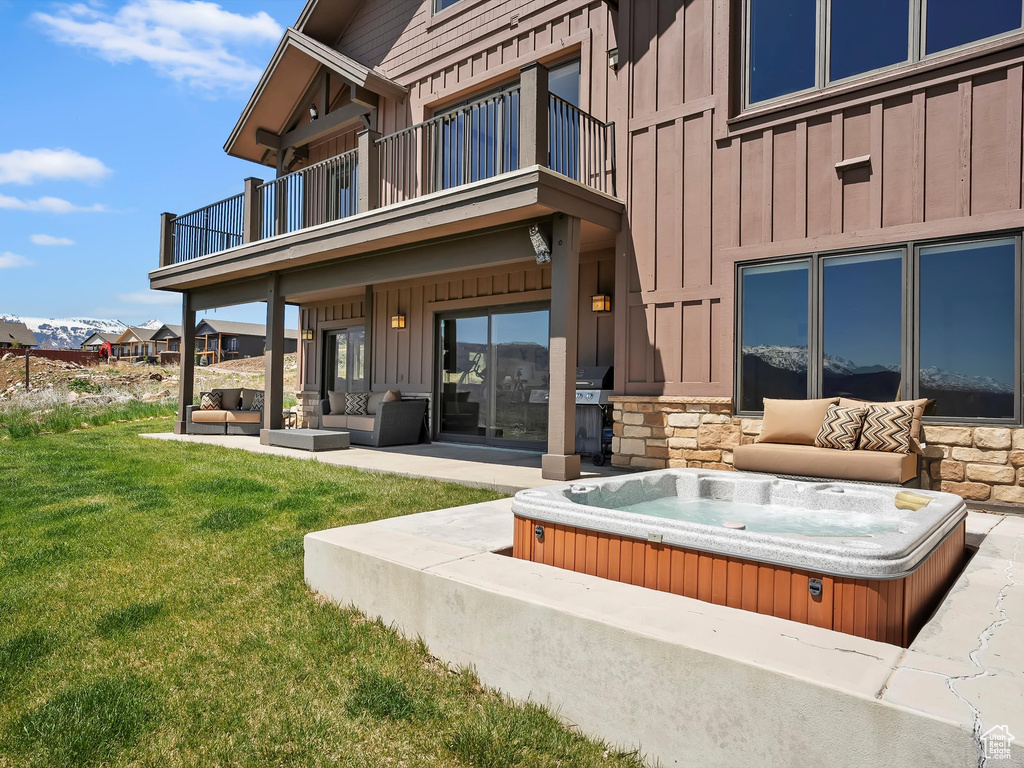 Exterior space featuring a lawn, an outdoor hot tub, board and batten siding, a balcony, and an outdoor hangout area