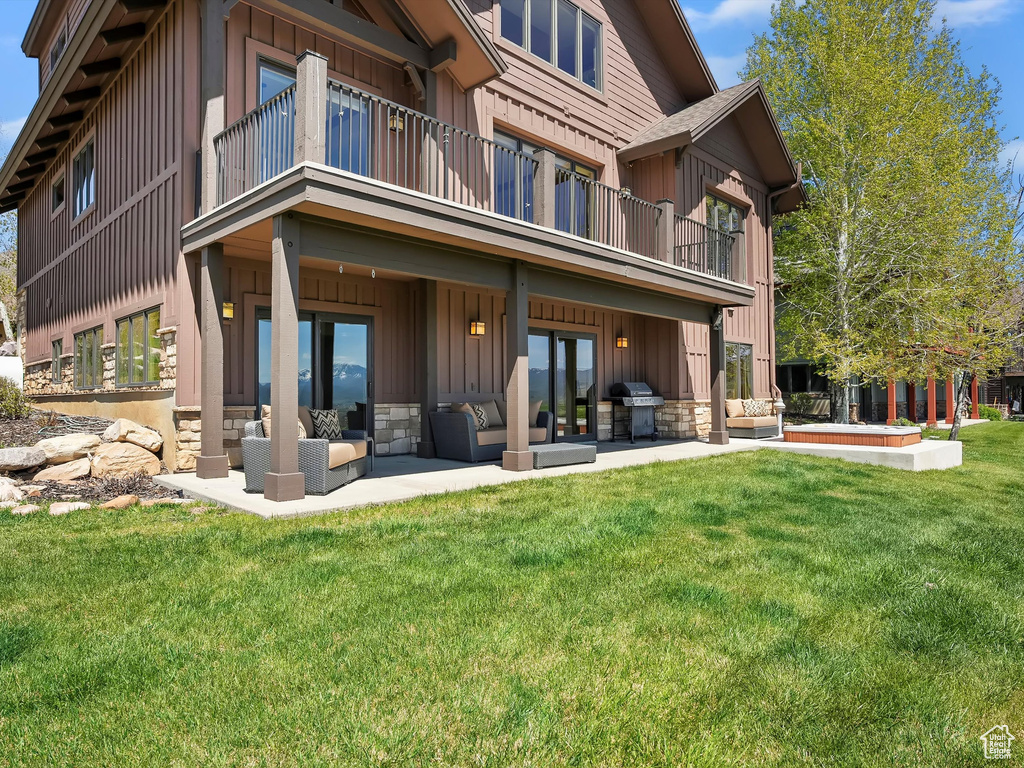 Back of property featuring a patio, board and batten siding, a balcony, an outdoor hangout area, and a yard