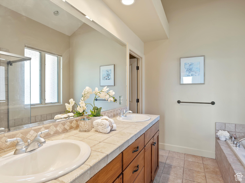 Full bath featuring a sink, double vanity, a garden tub, and baseboards