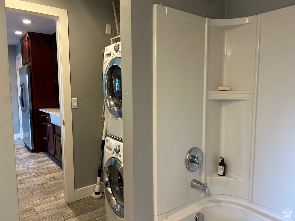 Laundry area featuring laundry area, stacked washer and dryer, baseboards, and light wood finished floors