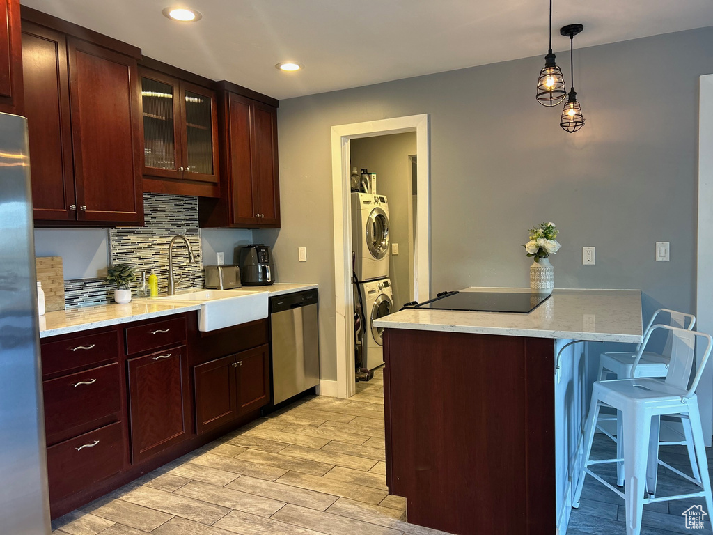 Kitchen with a breakfast bar area, stacked washing maching and dryer, a peninsula, backsplash, and stainless steel appliances