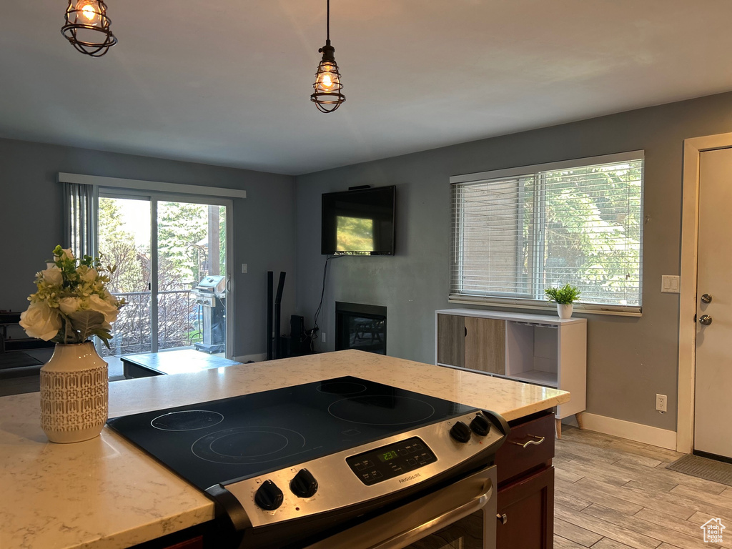 Kitchen with light stone countertops, light wood-style flooring, baseboards, hanging light fixtures, and electric range