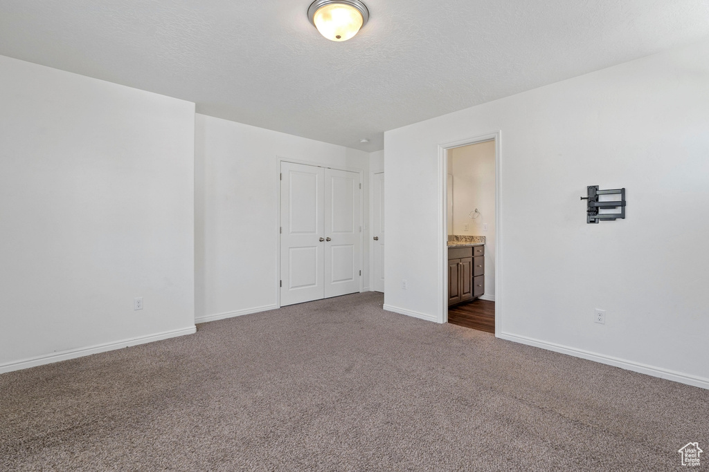 Unfurnished bedroom featuring a closet, a textured ceiling, baseboards, dark colored carpet, and connected bathroom