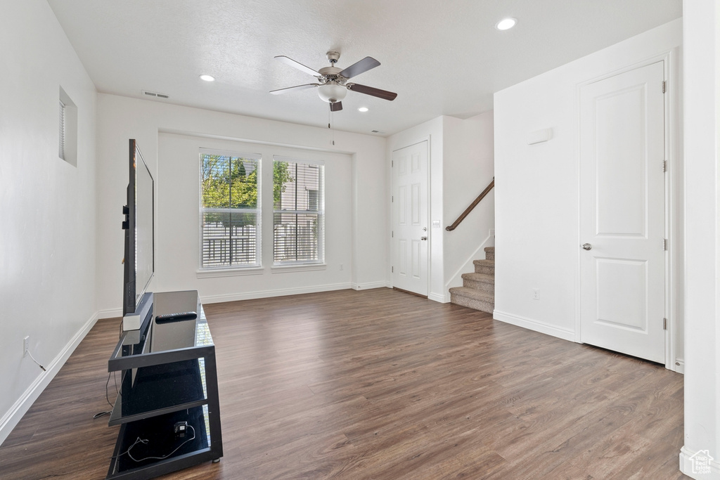 Unfurnished living room with wood finished floors, visible vents, baseboards, stairway, and ceiling fan