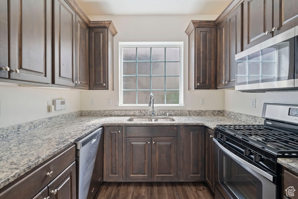 Kitchen featuring light stone countertops, dark wood-style flooring, a sink, dark brown cabinetry, and appliances with stainless steel finishes