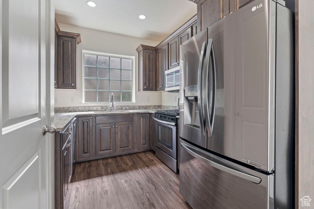 Kitchen with a sink, dark brown cabinetry, dark wood-style floors, light stone countertops, and appliances with stainless steel finishes