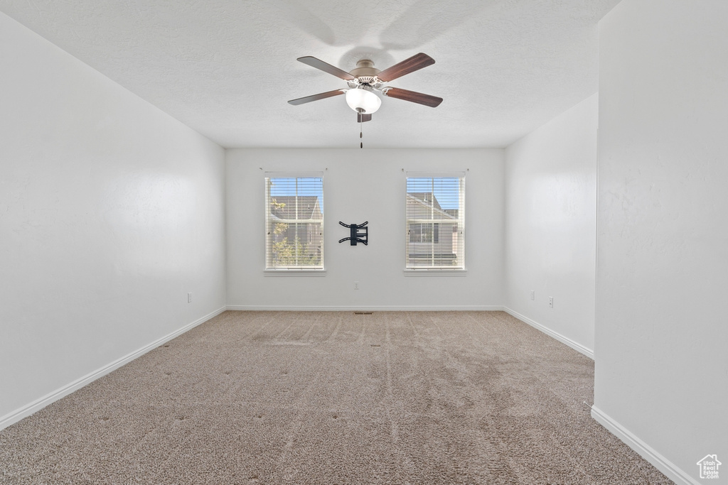 Unfurnished room with a textured ceiling, light carpet, baseboards, and a ceiling fan
