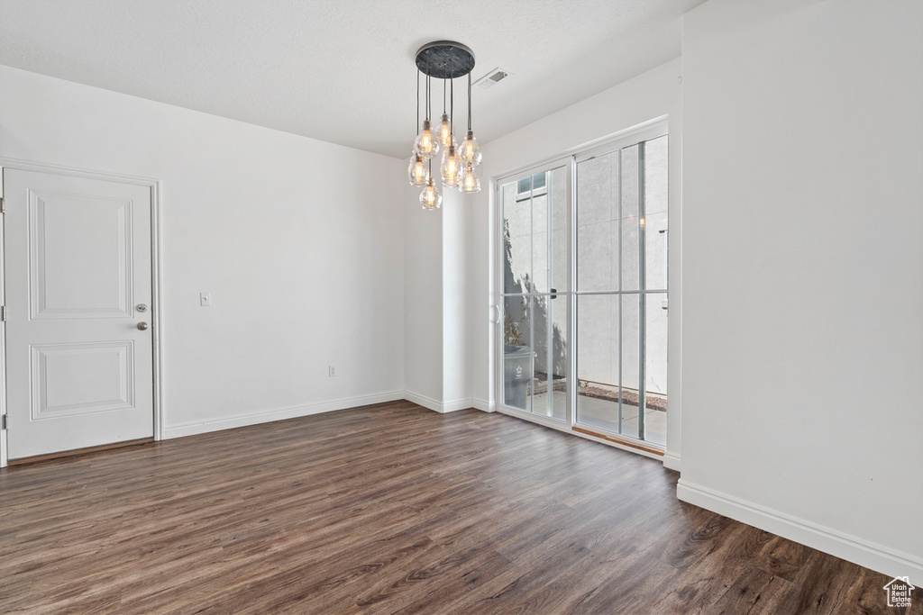 Unfurnished dining area featuring baseboards, a notable chandelier, dark wood finished floors, and visible vents