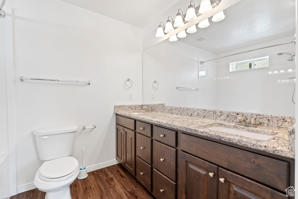 Bathroom featuring a sink, walk in shower, toilet, wood finished floors, and baseboards