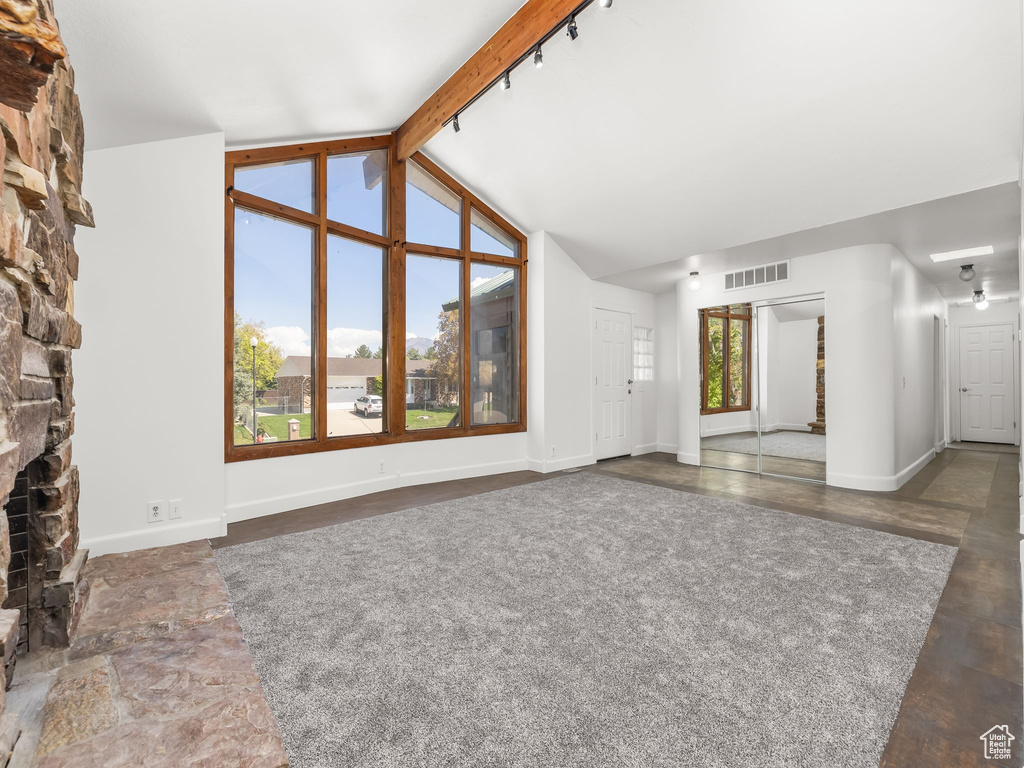 Unfurnished living room featuring baseboards, visible vents, vaulted ceiling with beams, and a fireplace
