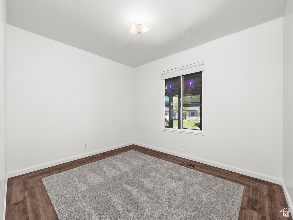 Unfurnished room featuring baseboards, dark wood-style floors, and visible vents