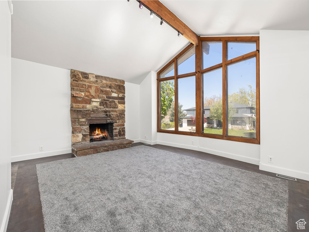 Unfurnished living room featuring baseboards, vaulted ceiling with beams, a stone fireplace, and visible vents