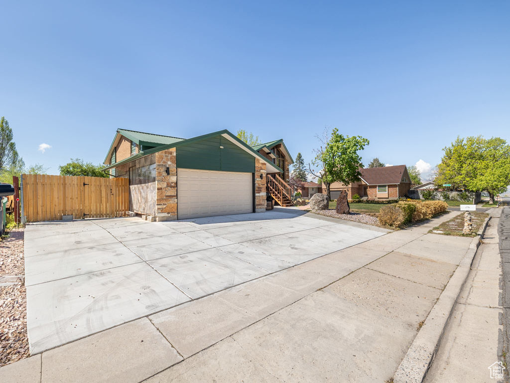 View of front of property with fence, stone siding, a gate, concrete driveway, and an attached garage