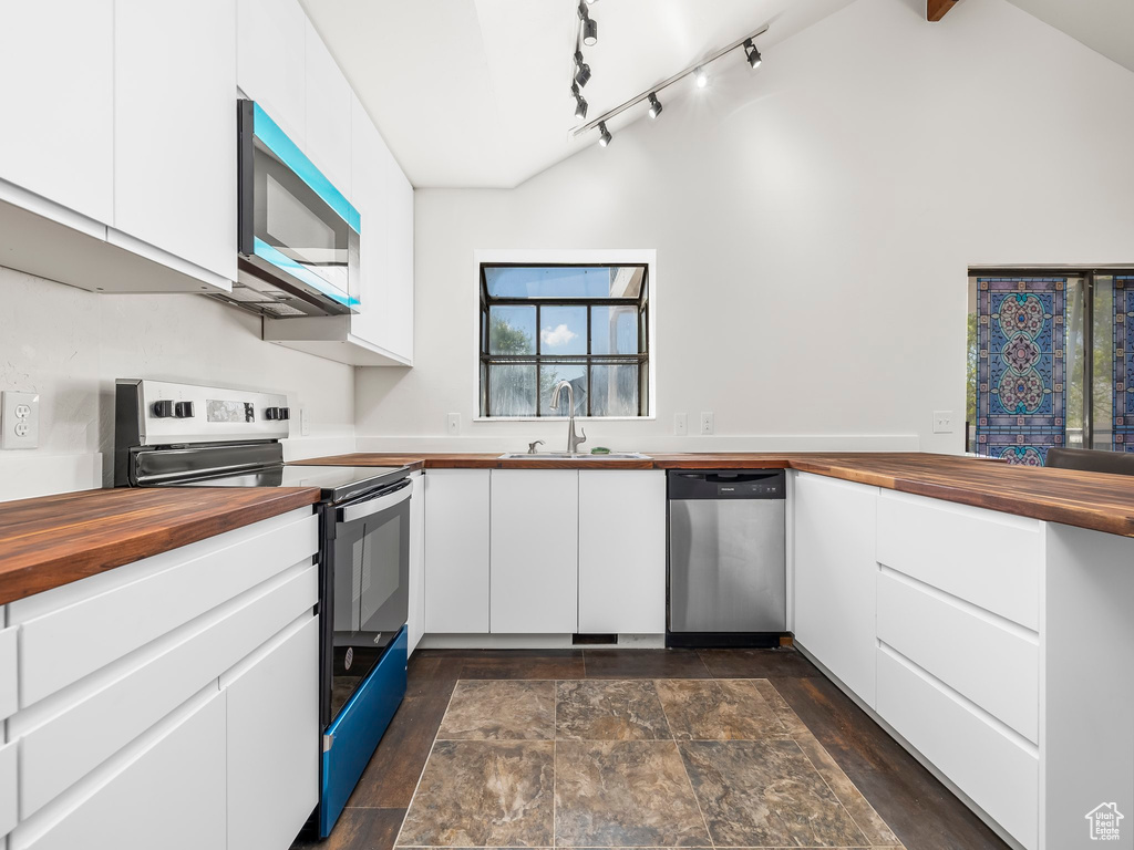 Kitchen featuring butcher block counters, white cabinets, a sink, vaulted ceiling, and stainless steel appliances