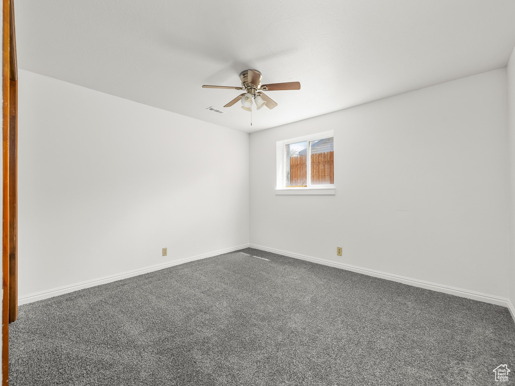Empty room with baseboards, ceiling fan, visible vents, and dark carpet