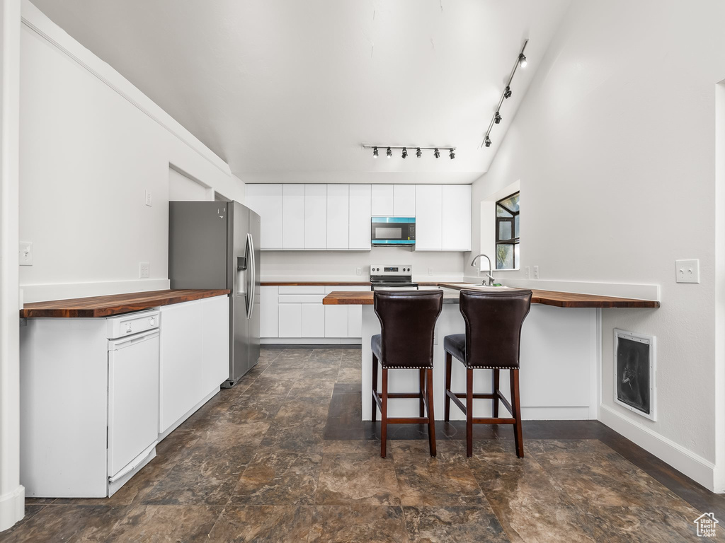 Kitchen featuring white cabinets, a breakfast bar area, rail lighting, stainless steel appliances, and butcher block counters