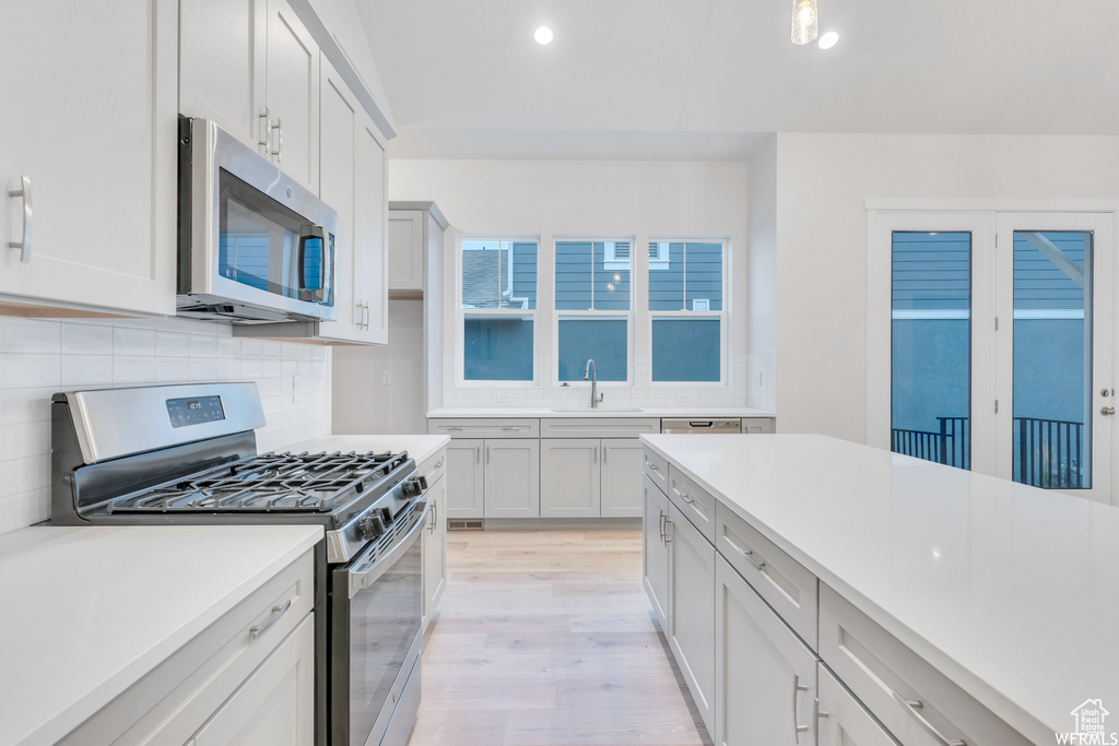 Kitchen with a sink, stainless steel appliances, light wood finished floors, backsplash, and light countertops