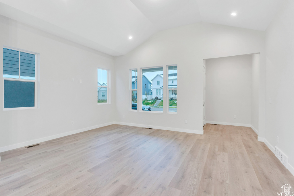 Empty room with lofted ceiling, light wood-style floors, and visible vents