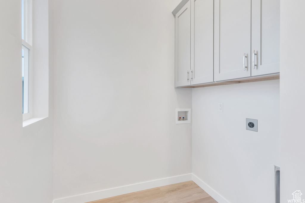 Laundry room featuring light wood finished floors, cabinet space, hookup for an electric dryer, hookup for a washing machine, and baseboards