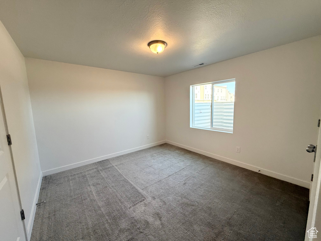 Empty room with baseboards, dark colored carpet, visible vents, and a textured ceiling