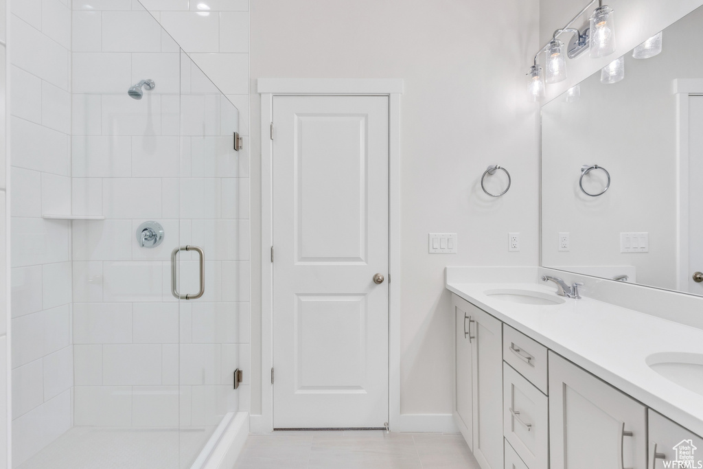 Full bath with double vanity, baseboards, a stall shower, and a sink