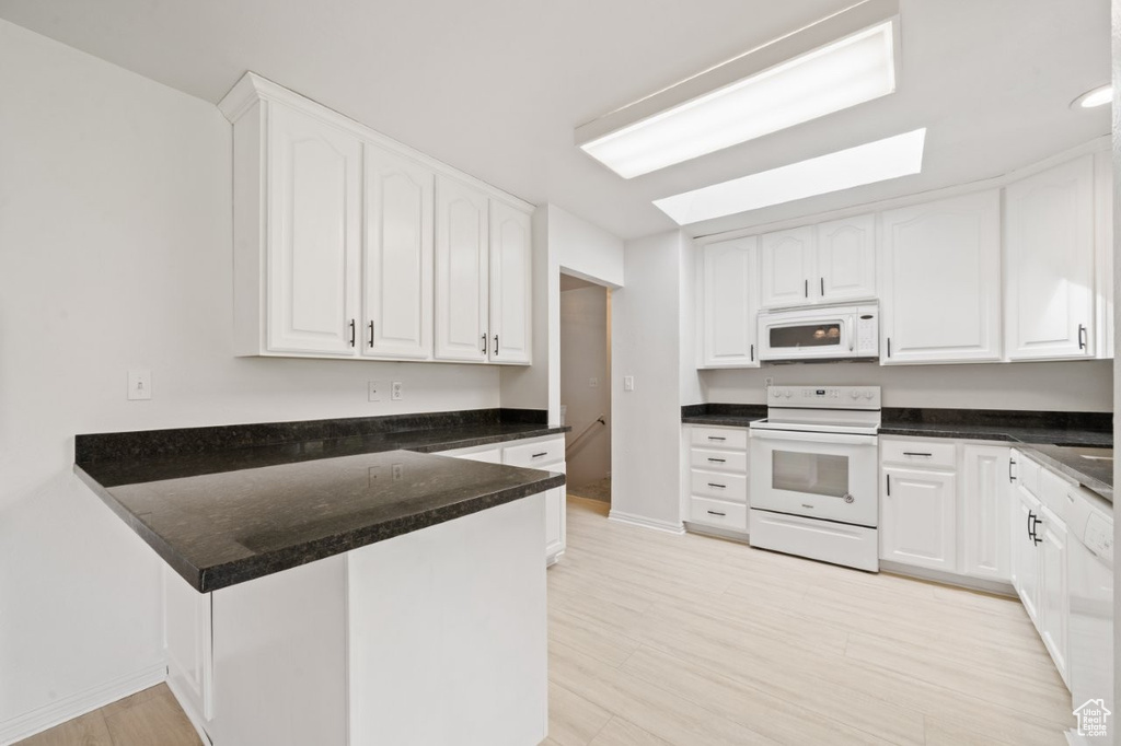 Kitchen with baseboards, white appliances, light wood finished floors, white cabinetry, and a peninsula