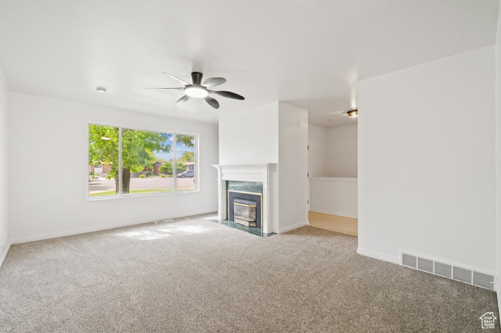 Unfurnished living room with a premium fireplace, ceiling fan, visible vents, and carpet floors
