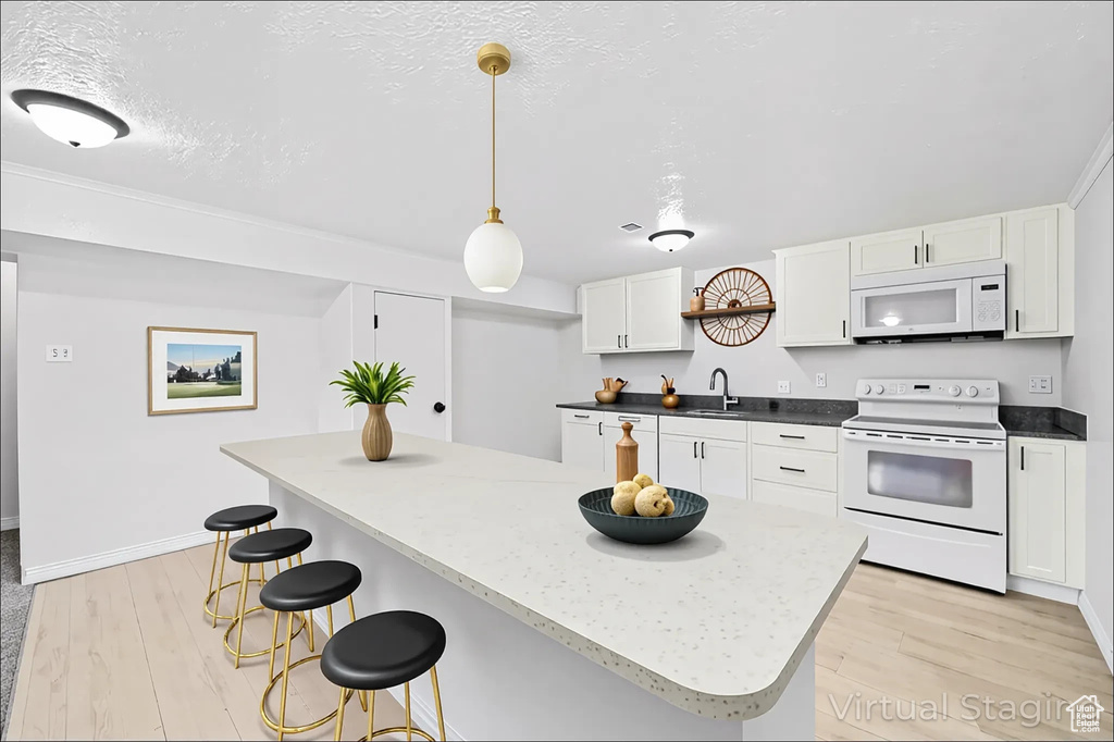 Kitchen featuring white appliances, light wood finished floors, a kitchen bar, and white cabinetry
