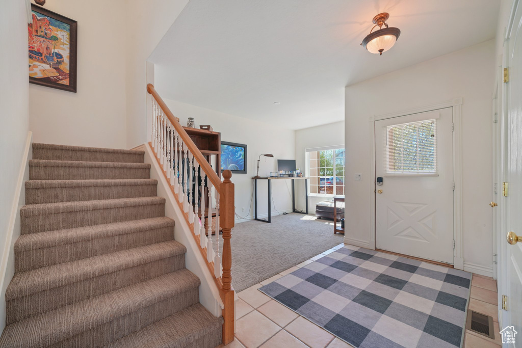 Foyer featuring stairs, light colored carpet, light tile patterned floors, and visible vents