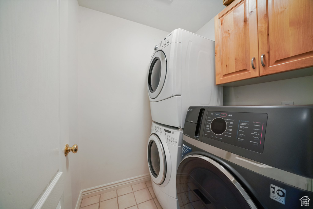 Laundry room featuring cabinet space, tile patterned floors, baseboards, and stacked washer / dryer