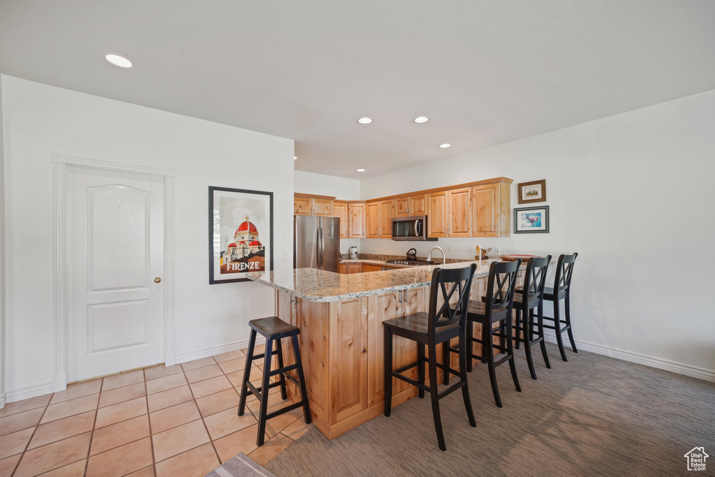 Kitchen with appliances with stainless steel finishes, baseboards, light stone counters, a peninsula, and a breakfast bar