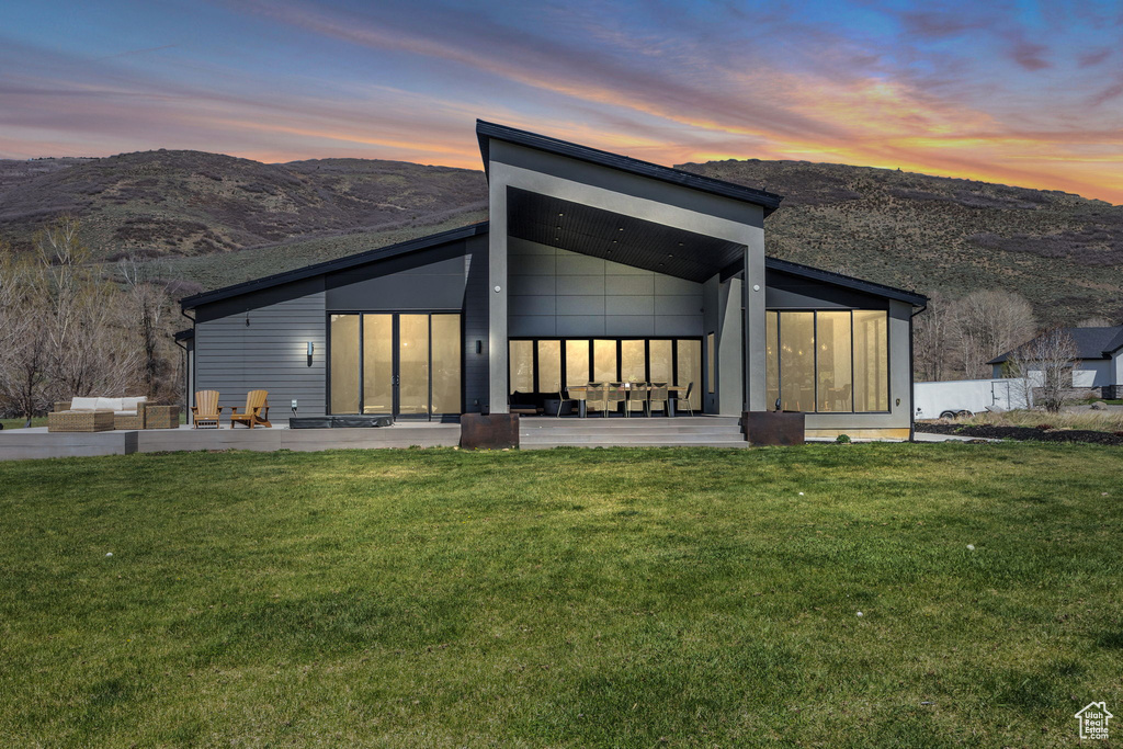 Back of property featuring a mountain view, a lawn, a patio, and a sunroom