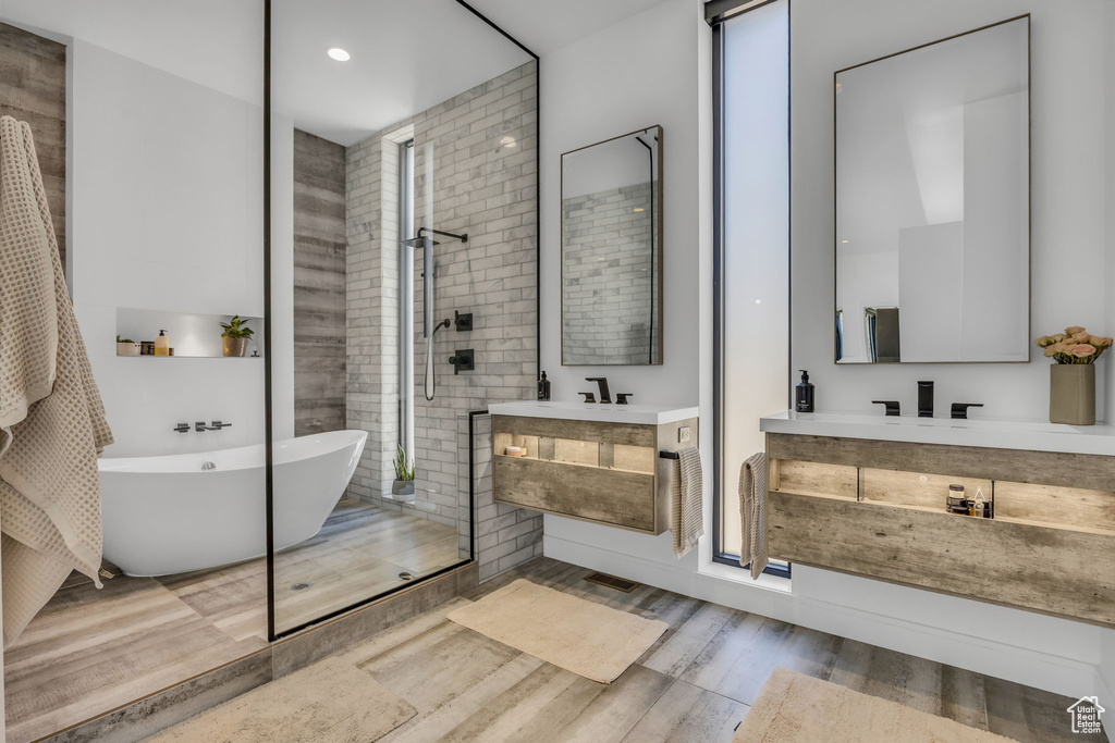 Full bathroom with wood finished floors, tiled shower, two vanities, a soaking tub, and recessed lighting