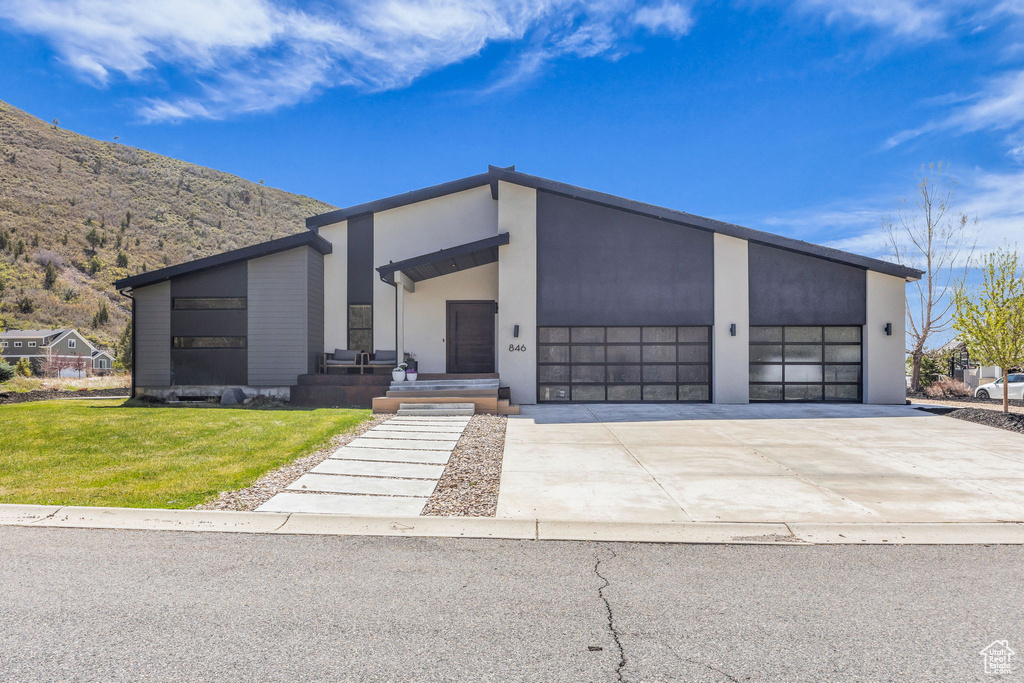 Modern home with concrete driveway, an attached garage, a front lawn, a mountain view, and stucco siding