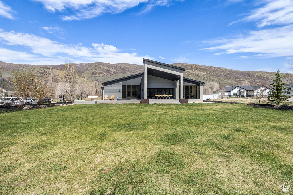 Back of house with a mountain view and a lawn