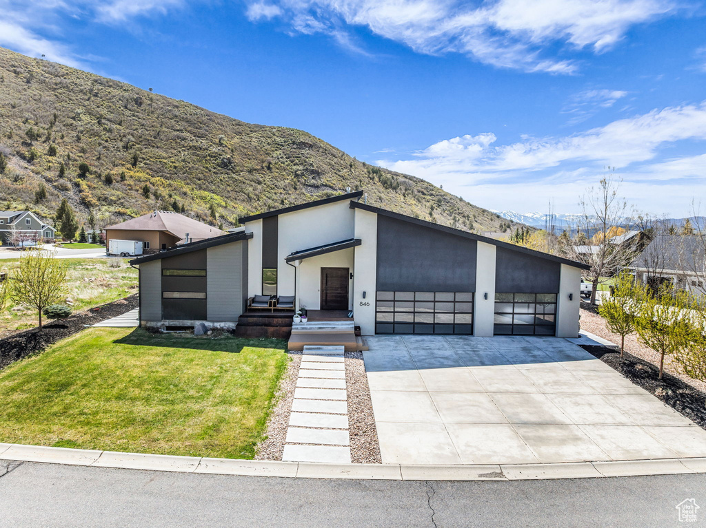 View of front of property featuring a mountain view, a front lawn, driveway, and an attached garage