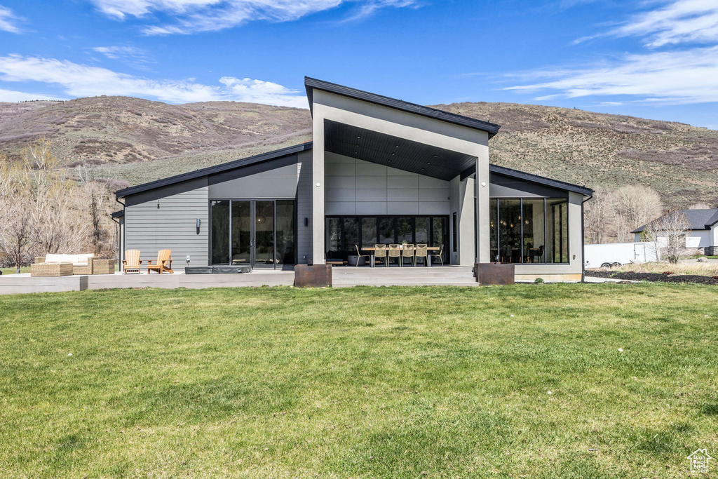 Rear view of house with a mountain view, a sunroom, a lawn, and a patio
