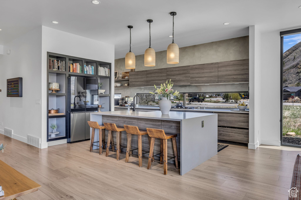 Kitchen with modern cabinets, light wood finished floors, a kitchen island with sink, light countertops, and a breakfast bar area