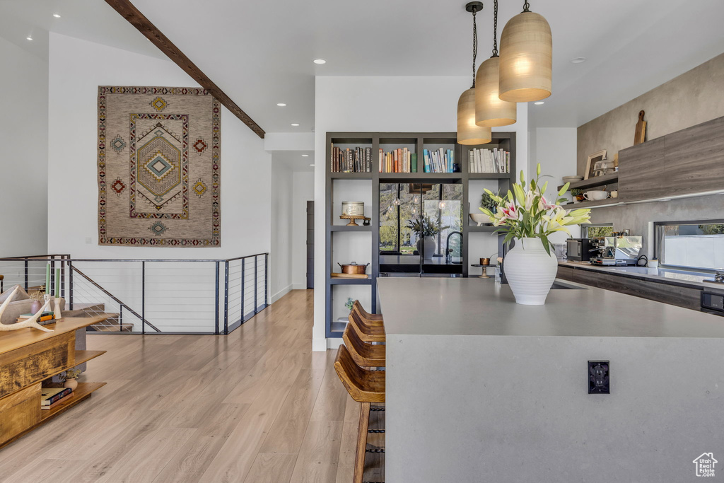 Kitchen with open shelves, light wood-style floors, pendant lighting, recessed lighting, and a breakfast bar