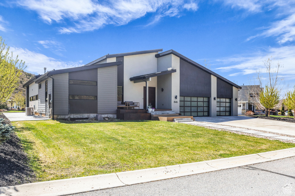 View of front facade with driveway, a front lawn, cooling unit, and an attached garage