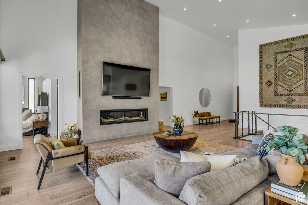 Living room with a towering ceiling, light wood-type flooring, a premium fireplace, baseboards, and recessed lighting