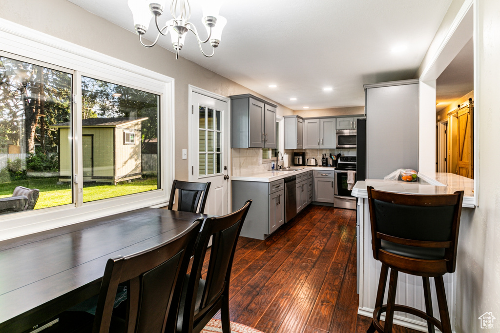 Kitchen with a sink, a chandelier, light countertops, gray cabinetry, and appliances with stainless steel finishes