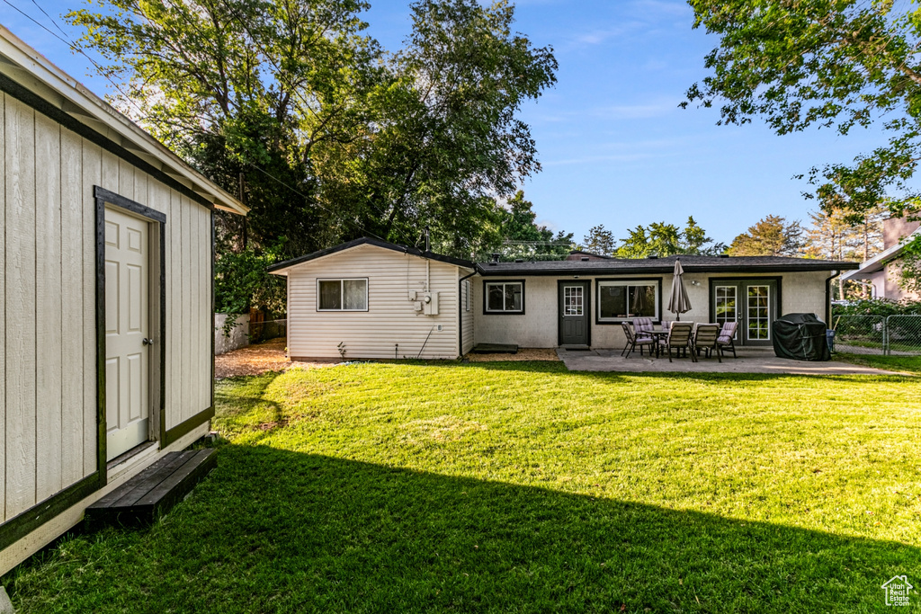 Back of house featuring a fenced backyard, a patio, an outbuilding, and a lawn